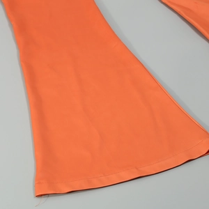 Detailed close-up of bright orange flare pants hem showing smooth fabric and stitching