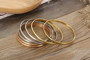 Stack of gold, silver and rose gold polished titanium steel bangles on wood surface
