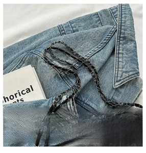 Detail of black PU leather shoulder bag with metallic chain strap on denim background