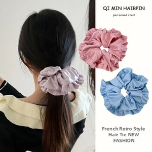 Close-up of three satin hair scrunchies in lilac, pink, and blue with soft pleats