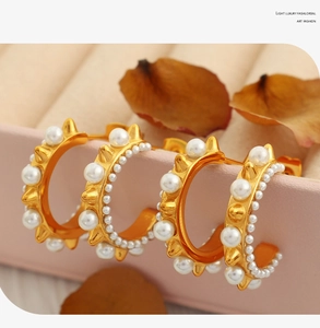 Detail of gold C-shaped earrings with pearls and metallic spikes on a pink display