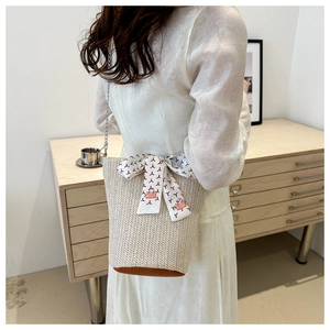 Détail du sac seau en paille beige avec base en cuir et foulard en soie décoratif