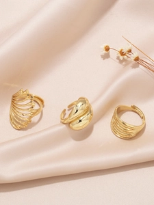 Close-up of gold-plated feather and textured adjustable stackable rings set on satin