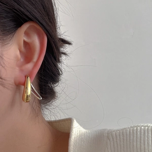 Close-up of elegant gold and silver teardrop earrings worn by a model in soft light