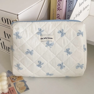 Quilted makeup bag with blue bows and jolly house label on a decorative desk