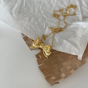Detailed view of a polished gold bow necklace elegantly placed on gift wrapping paper