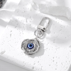 Detail of silver rose keychain with blue evil eye bead on a textured stone surface