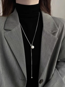 Detail of elegant silver Y-shape long necklace with white pearl on black turtleneck