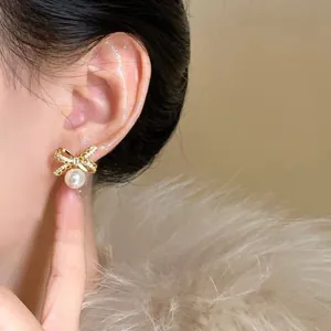 Detail of 18K gold plated bow earrings with sparkling cubic zirconia and hanging pearl