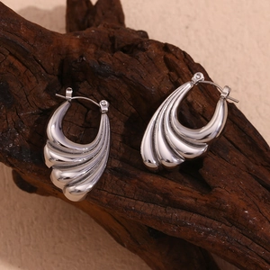 Macro detail of silver wave earrings with textured grooves on natural wood display