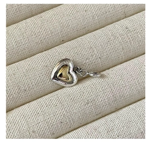 Macro shot of two-tone heart pendant in silver and gold on a beige textured fabric