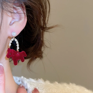 Detailed view of red flocked horse earrings with pearl accents worn by a model