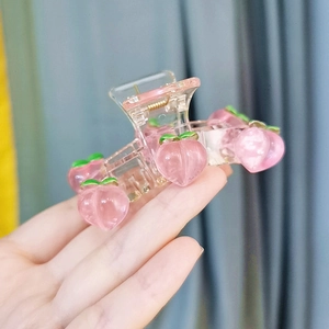 Detail showing a pink peach resin hair claw clip with green leaves held in hand