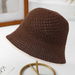 Detail of a brown open-weave summer bucket hat with contrast cream trim on a metal stand