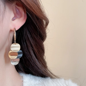 Close-up of model wearing layered gold, black, and silver metal disc earrings with a matte finish