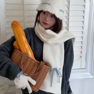 Detail of cream knit scarf and hat set with elegant blue bow accents on the fabric