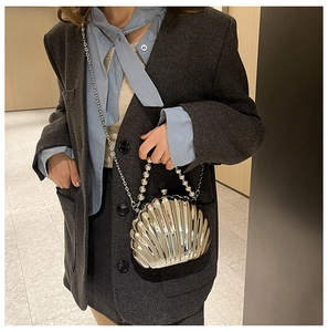 Silver shell clutch with pearl handle and metal chain shown on a charcoal blazer