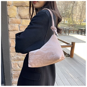 Close-up of pink tote bag with glossy pleated texture and knotted strap in outdoor setting