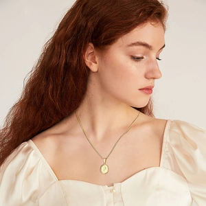 Elegant gold round pendant necklace with flower pattern worn by model on satin top