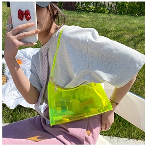 Neon yellow transparent PVC shoulder bag displayed outdoors on green grass with cosmetics