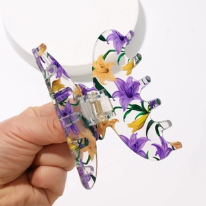 Close-up of a hand holding a transparent butterfly hair claw with purple lily prints