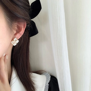 Elegant white floral stud earrings with gold trim worn by a model in natural light