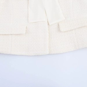 Detail of tweed jacket texture with smooth white fabric bow and pocket flaps on white