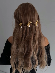 Trois barrettes dorées en nœud avec perles sur des cheveux bruns ondulés