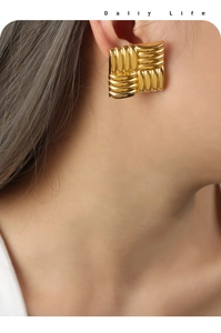 Close-up of golden square earrings with textured woven pattern on a female model