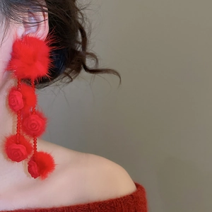 Close-up of model wearing red flower earrings with plush pom-pom and beaded tassels
