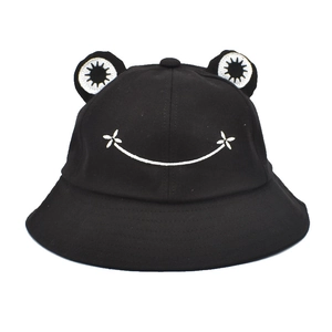 Detail of a black bucket hat with cartoon frog eyes and an embroidered smile on the front