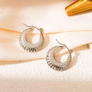 Detail view of silver scalloped hollow hoop earrings on beige satin and white stone