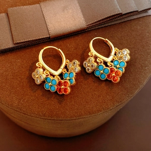 Macro shot of gold plated earrings featuring blue and red flower charms with zircon