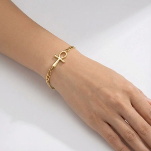 Detailed view of a gold-tone Ankh cross charm bracelet worn on a female wrist