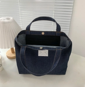 Detail of denim tote bag showing magnetic closure and interior pocket with bear patch