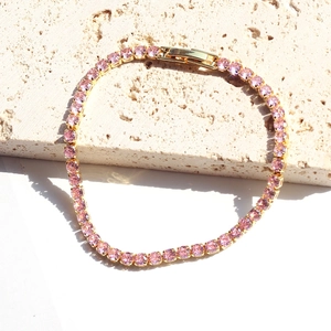 Detail of pink zircon tennis bracelet with gold finish on textured stone background