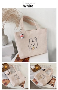 Detailed view of corduroy tote bag featuring rabbit embroidery and a cow plush charm