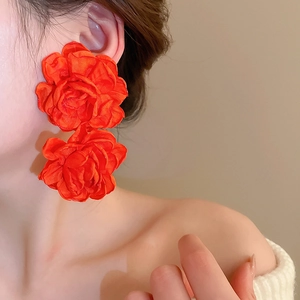 Detailed close-up of vibrant orange silk flower earrings worn by a model in warm light