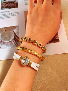 Detailed shot of gold link bracelet with gemstones and white leather crystal bangle set