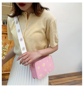 Close-up of a pink daisy crossbody bag with a wide floral shoulder strap on a model