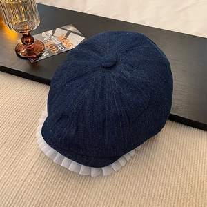 Detail of dark blue denim newsboy cap featuring elegant white lace trim on the brim