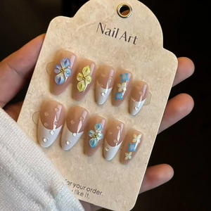 Detail of press-on nails with 3D floral accents, water droplets, and French tips on nude base
