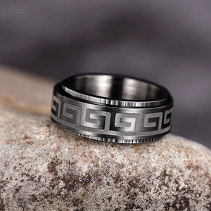 Macro shot of matte black stainless steel ring with Greek fret pattern on volcanic rock