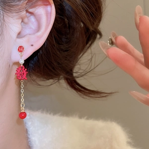 Détail de boucles d'oreilles rouges à pompons avec motif de caractère de bonheur