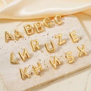 Golden 3D bubble initial earrings with polished metal finish on silk background