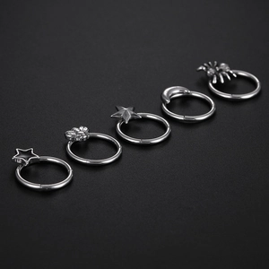 Macro detail of silver stainless steel nose rings with star, moon, and spider charms