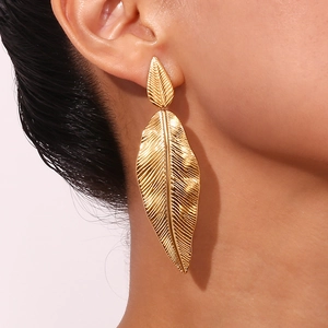 Detailed view of 18K gold leaf earrings with intricate feather texture worn by a model