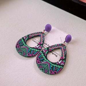 Detail of drop-shaped acrylic earrings with purple studs and pop art geometric patterns