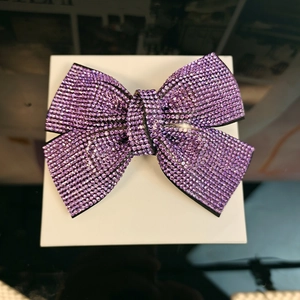 Close-up of sparkling purple rhinestone bow hair clip on white box with detailed shine