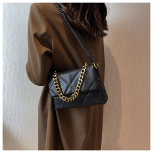 Détail du sac bandoulière matelassé noir avec chaîne dorée porté sur un manteau marron